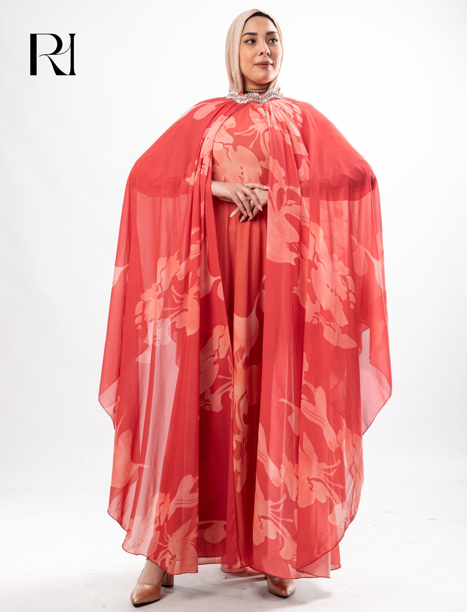Woman wearing a red floral dress with a sheer overlay on a white background, featuring the brand 'RI'.