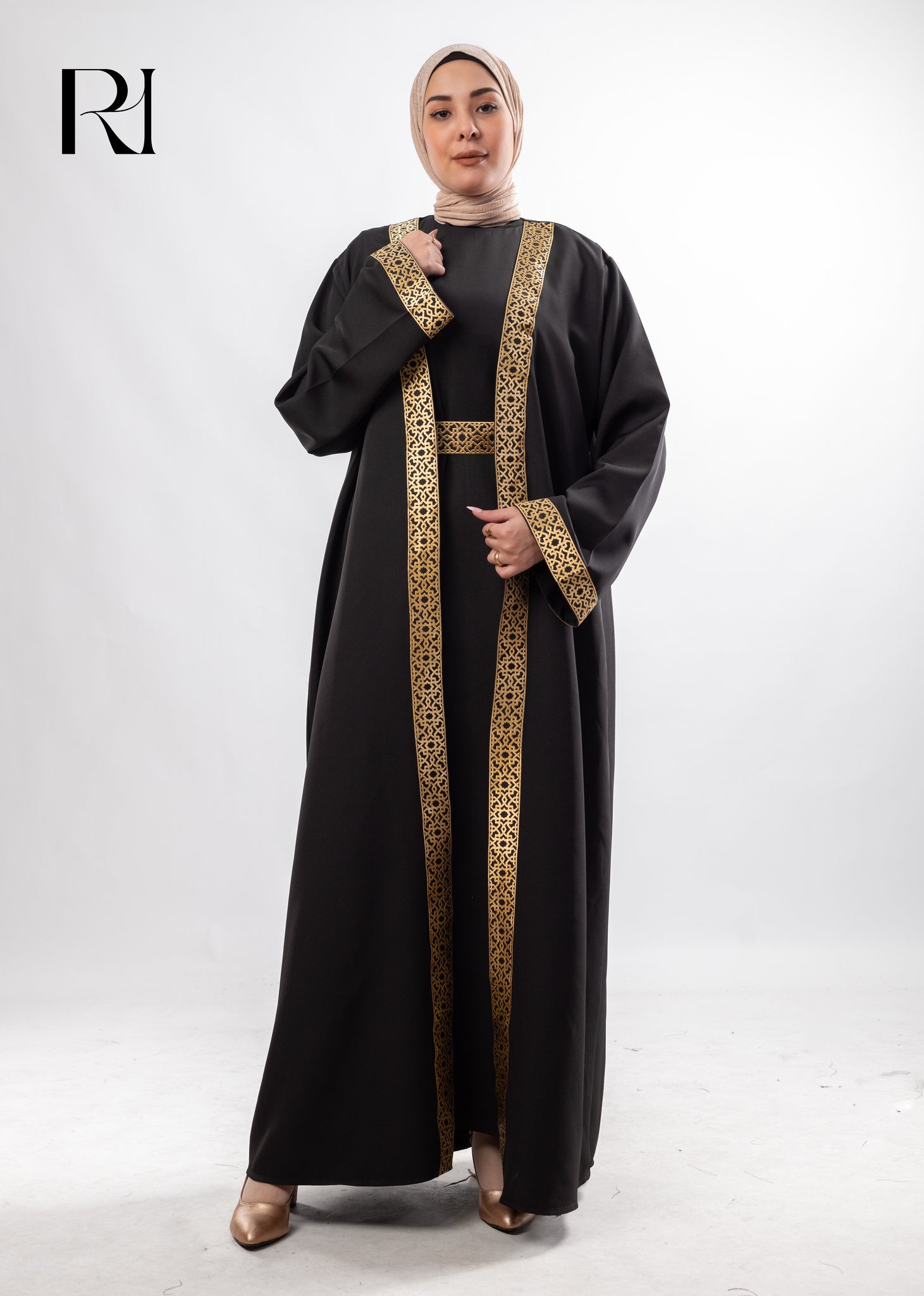 Woman wearing a black abaya with gold embroidery on a white background, featuring the brand 'RI'.