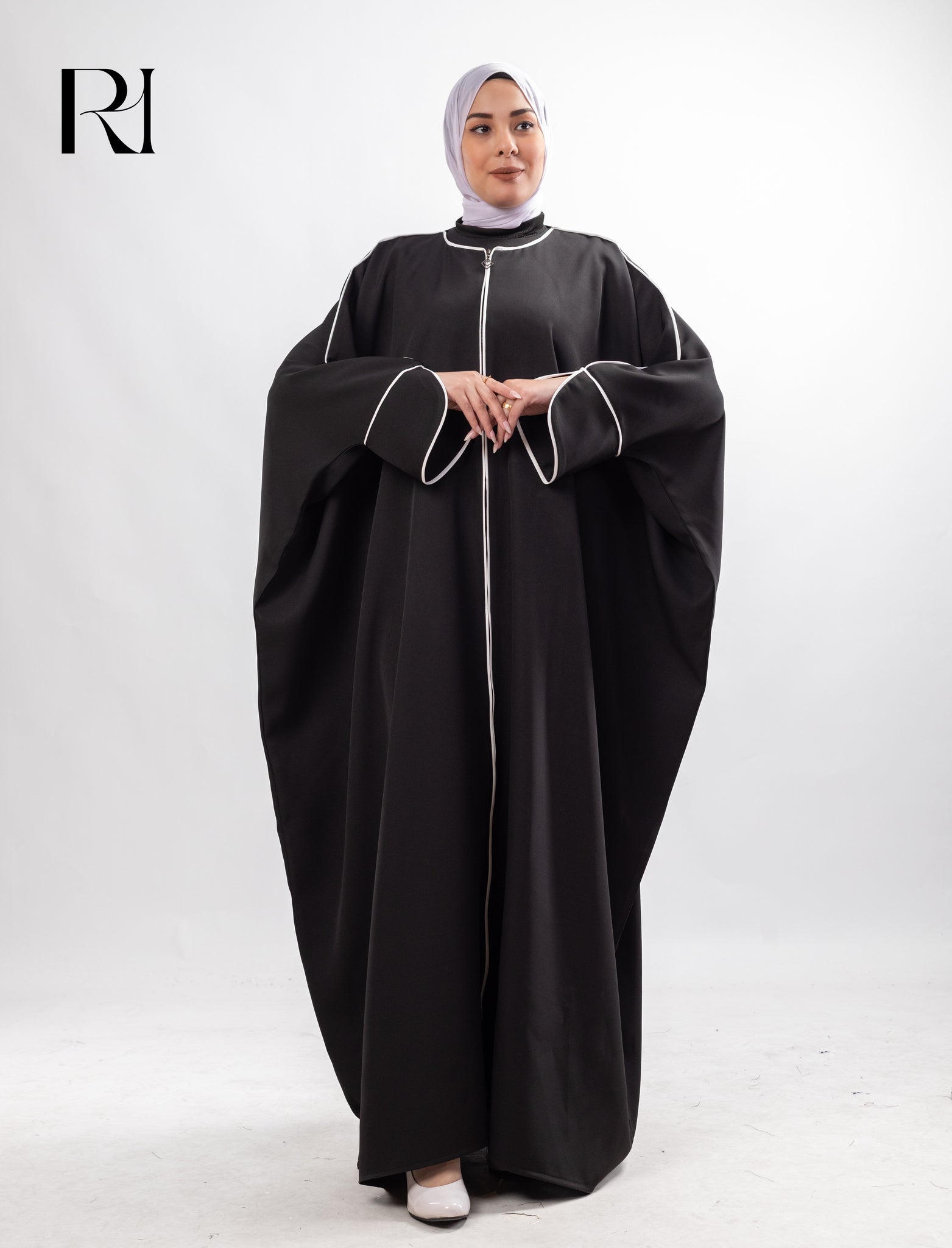 Woman wearing a black abaya with white trim on a white background, featuring the brand 'RI'.