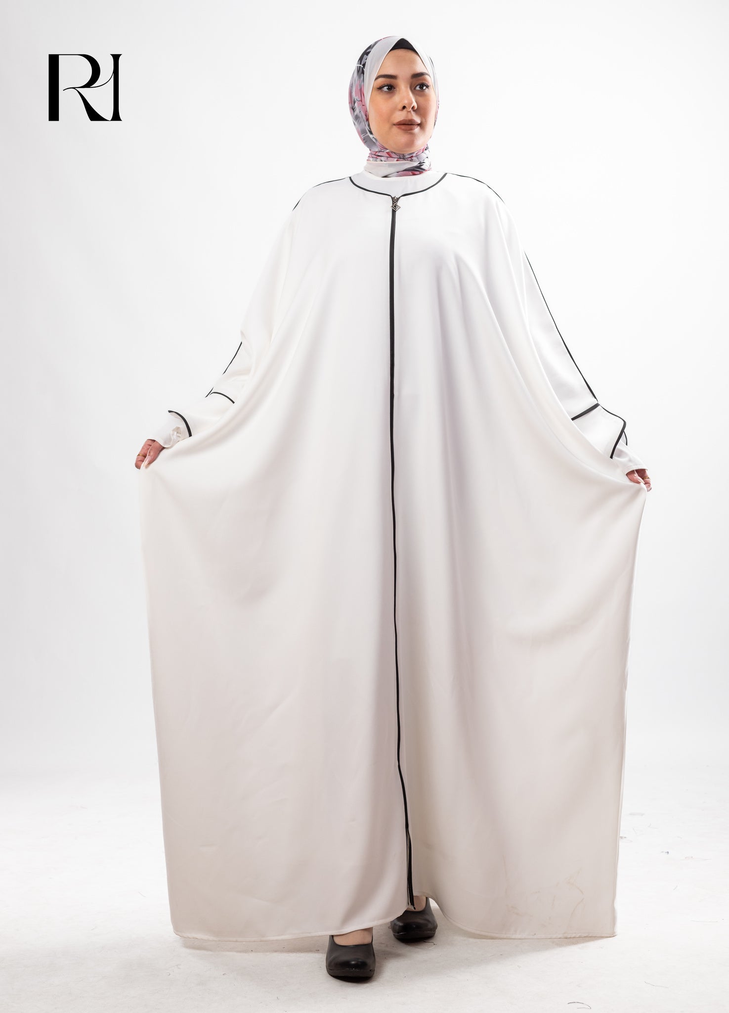 Woman wearing a white abaya with black trim on a white background, featuring the brand logo.