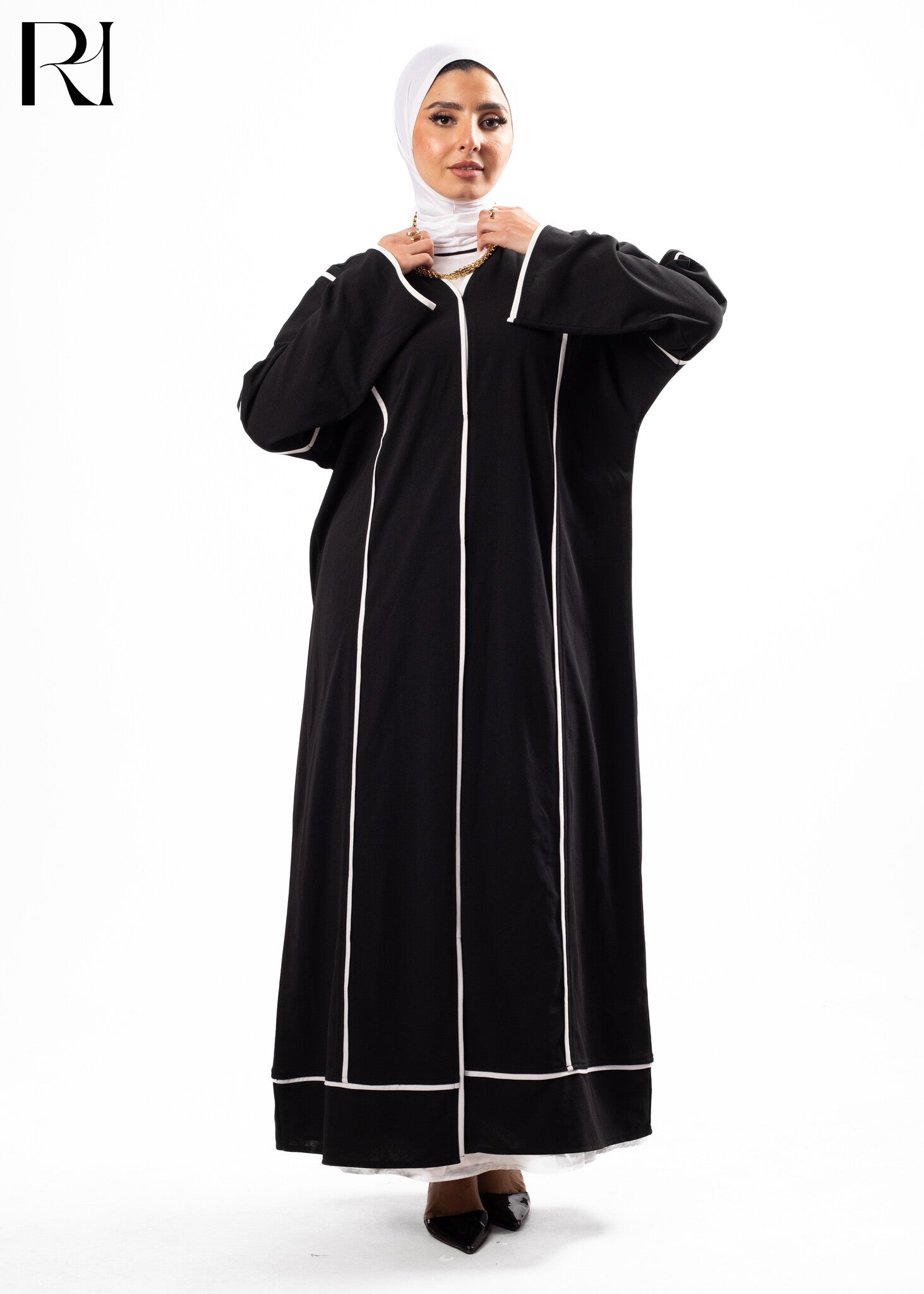 Woman wearing a black abaya with white trim on a white background