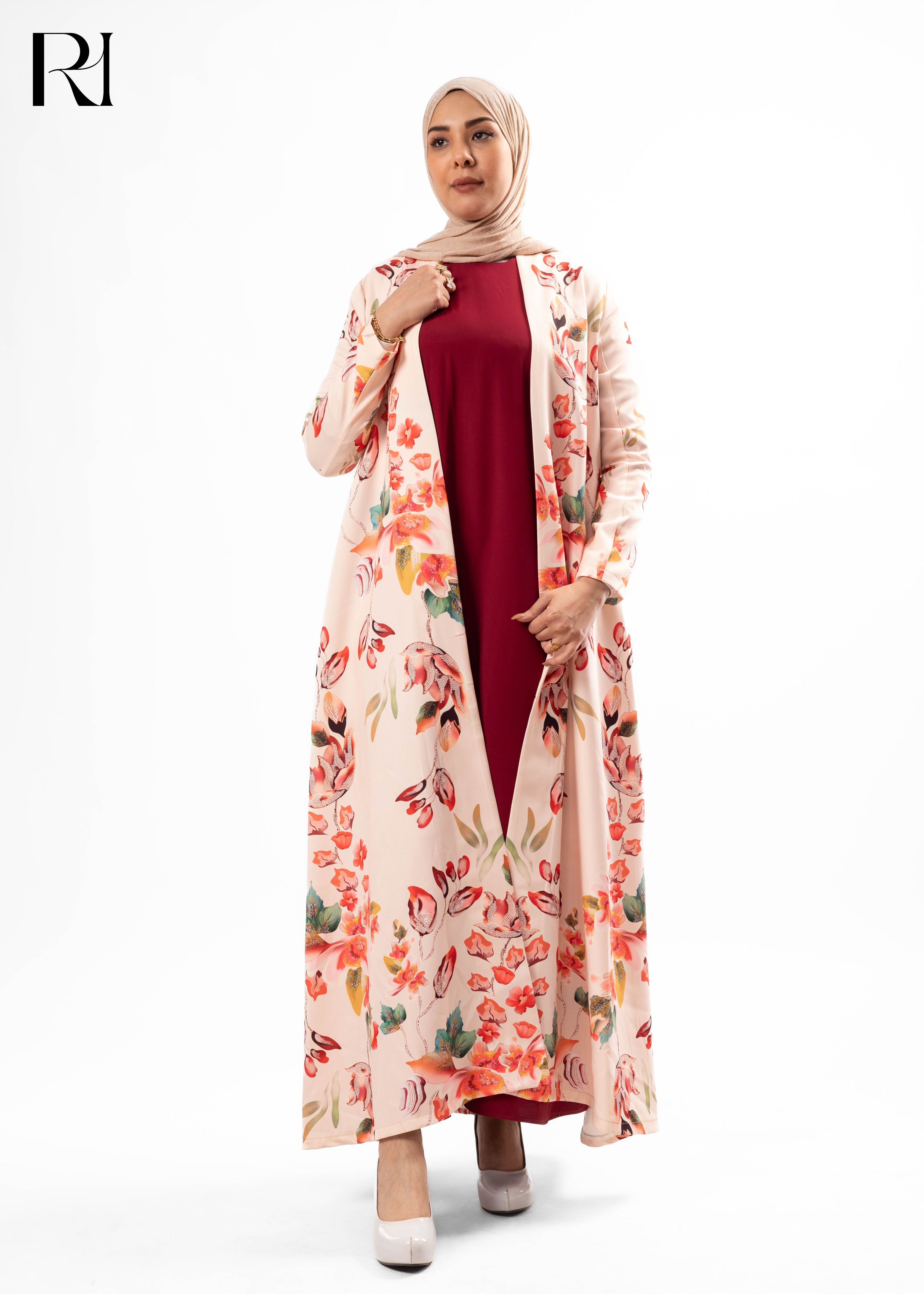 Woman wearing a floral dress over a red top with a hijab, on a white background.