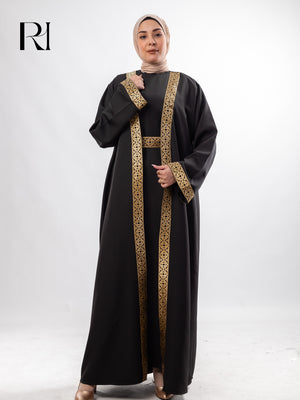Woman wearing a black abaya with gold embroidery on a white background, featuring the brand 'RI'.
