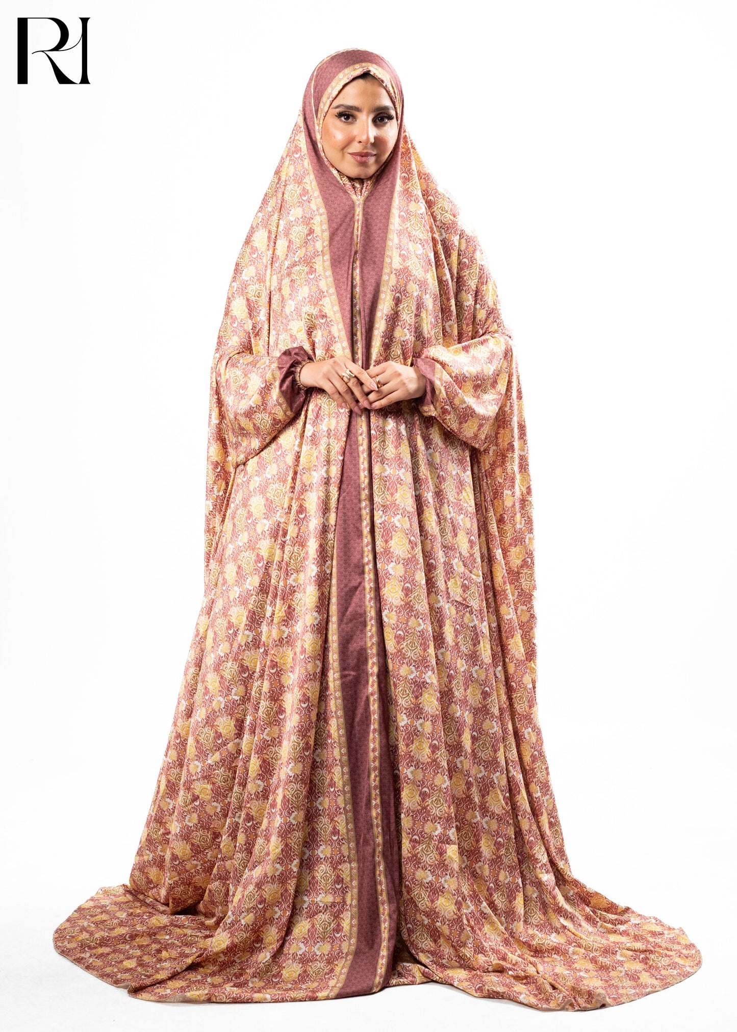Woman wearing a patterned abaya with a hijab on a white background, featuring the brand 'RI'.