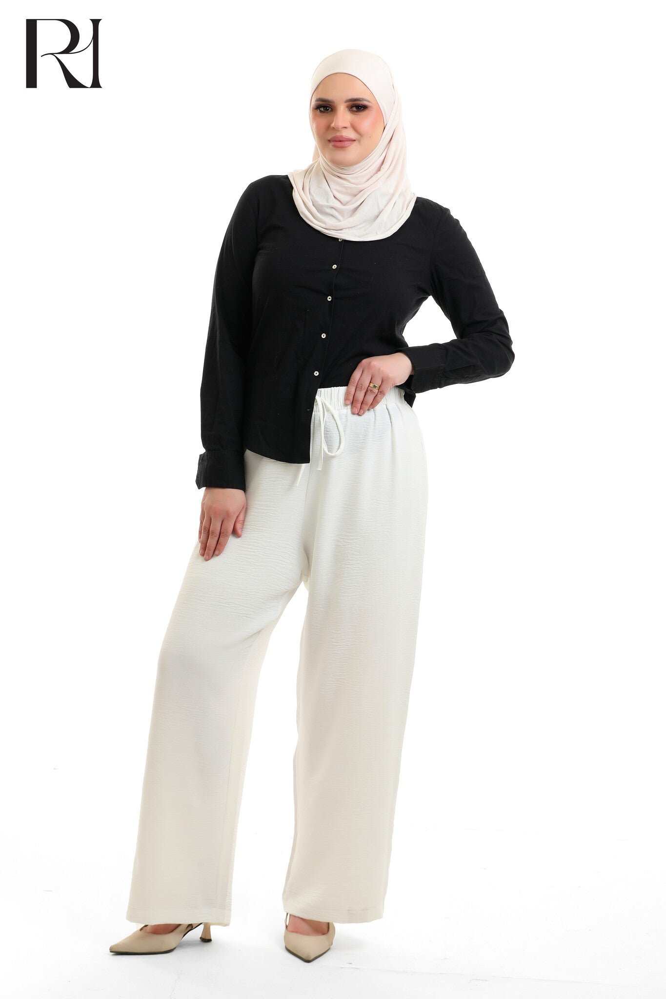 Woman wearing a black top and white hijab with wide-leg pants on a white background