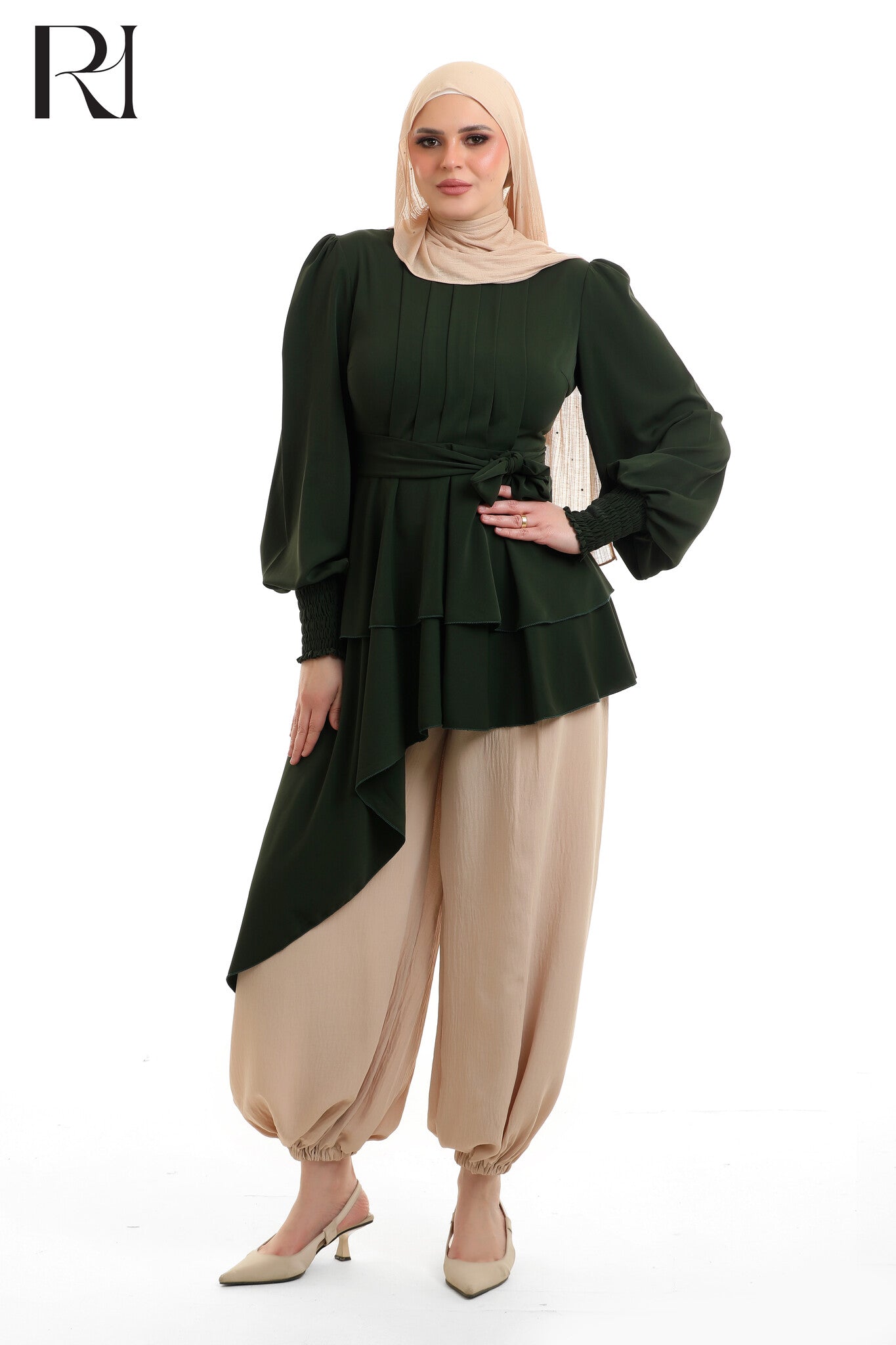 Woman wearing a green top and beige pants with a hijab on a white background