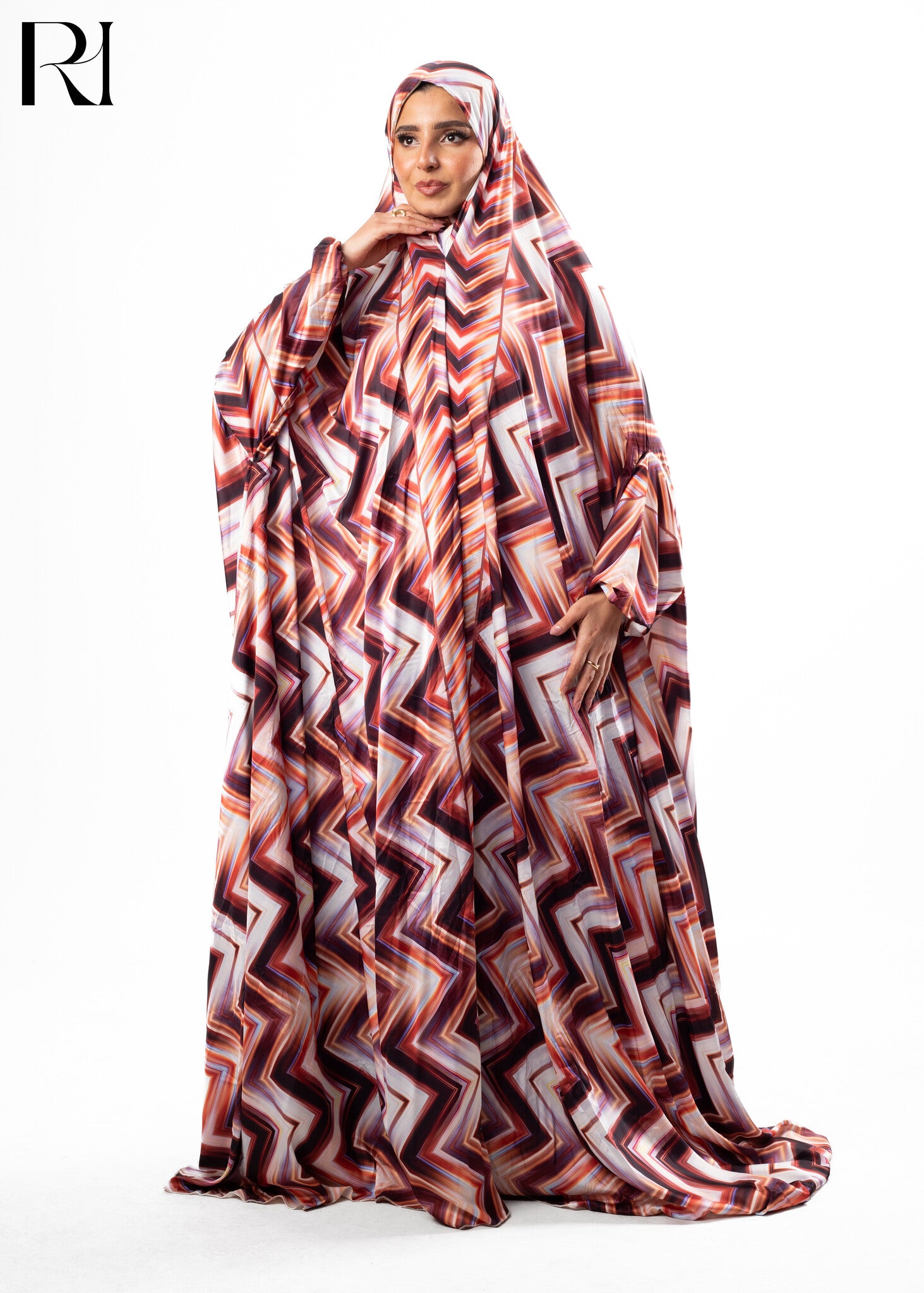 Woman wearing a patterned abaya with a visible brand logo on a white background